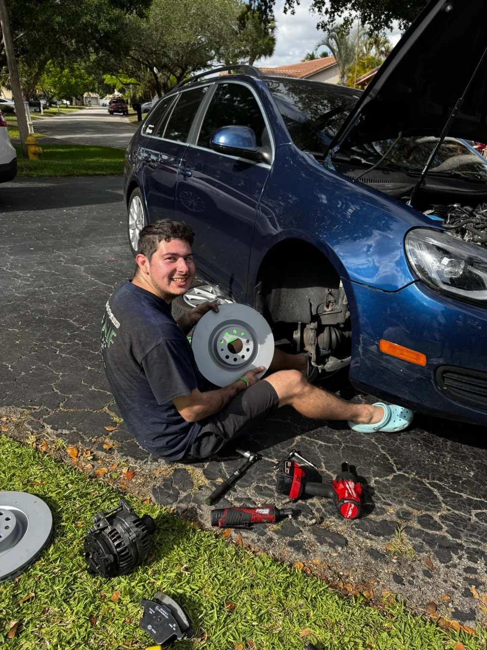 Josh holding a replacement brake rotor beside a car in a driveway